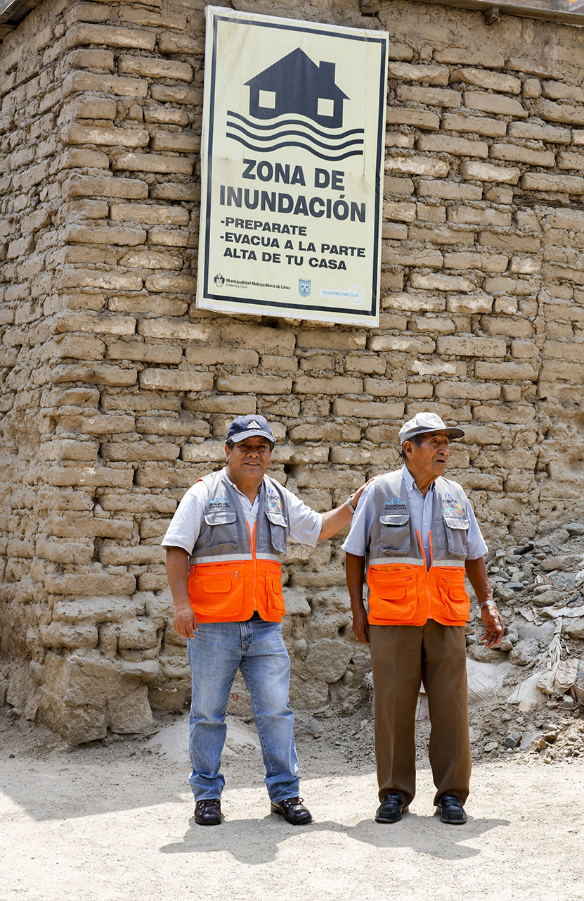 Brigadista and trainer in front of a flood sign, Chosica, Lima, Peru