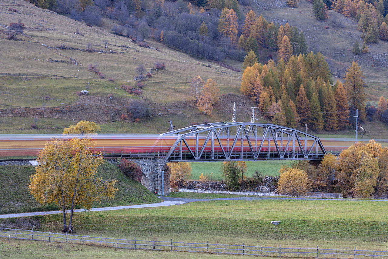 Beleuchteter Zug fährt über eine Eisenbahnbrücke, Rhätische Bahn, Zernez, Unterengadin, Graubünden, Schweiz